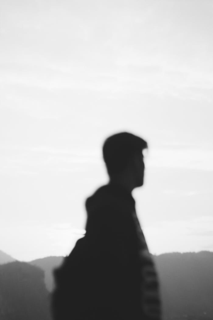 Black and white silhouette of a traveler with a backpack against a serene mountain landscape.