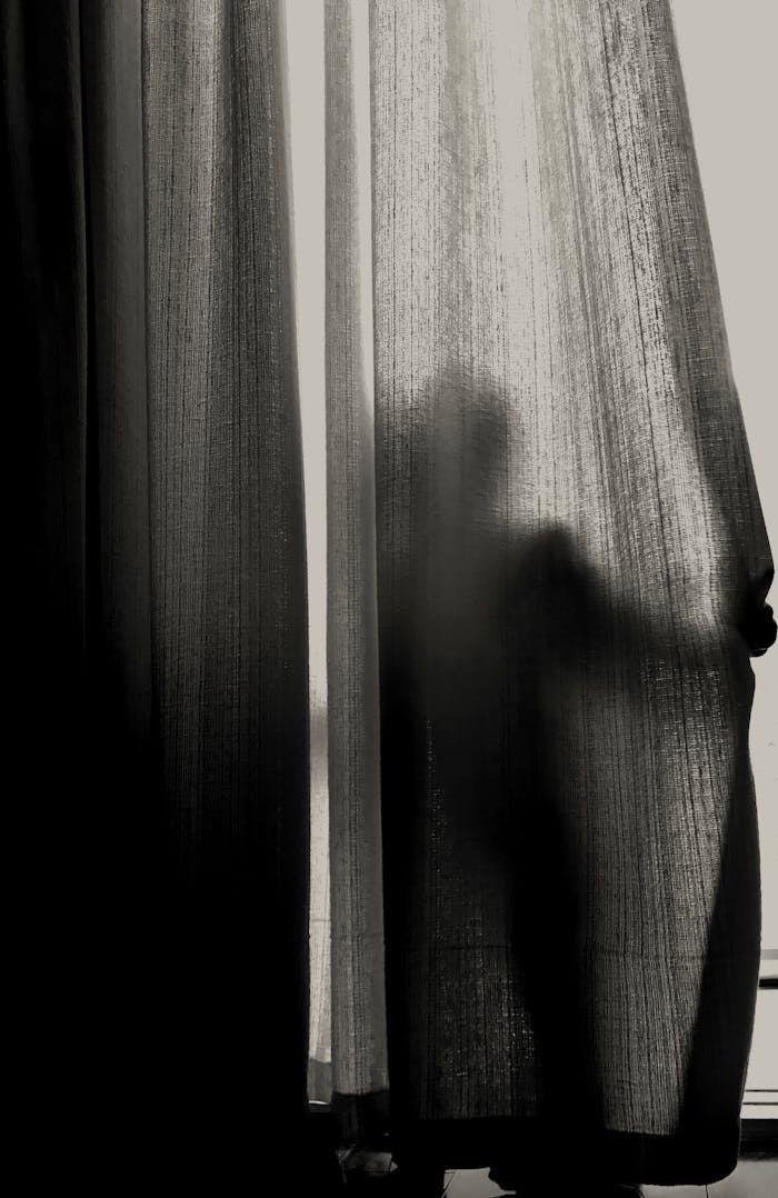 about-01 A mysterious silhouette of a person standing behind curtain in a dark room.