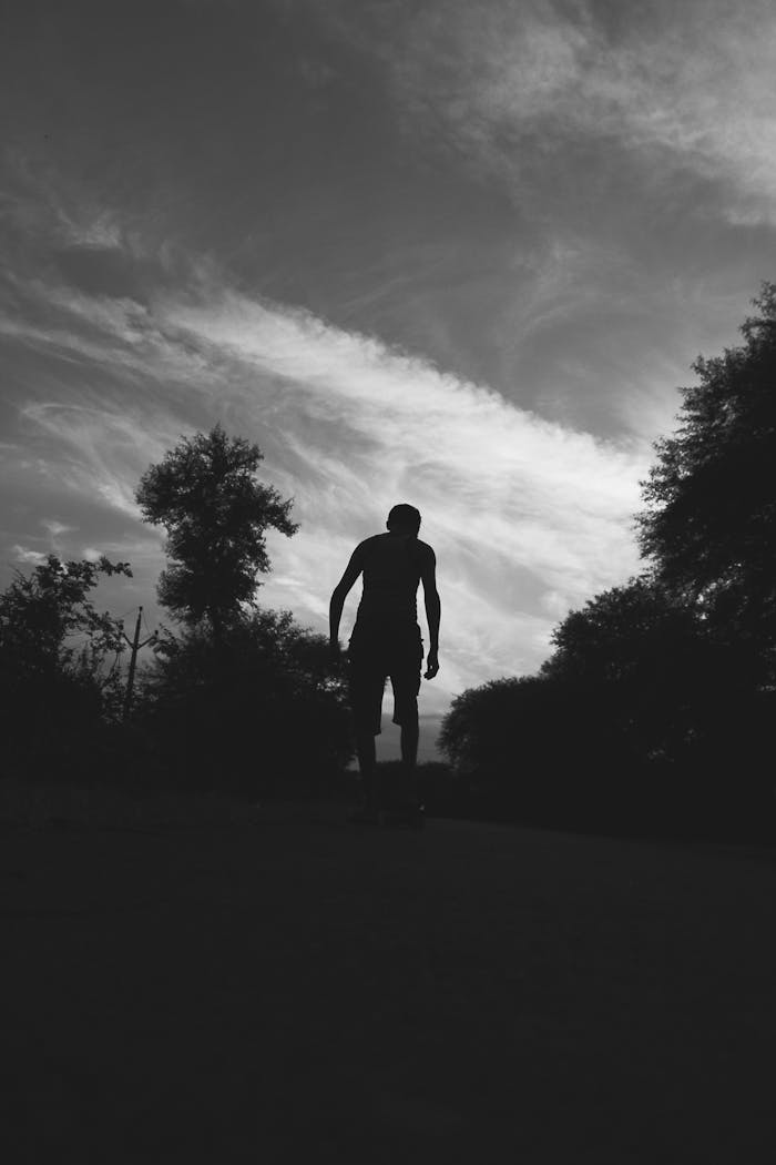 about-02 Dramatic black and white silhouette of a man walking with a skateboard against a cloudy sky.